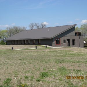 Building with angled gray roof on a grassy hill, with multiple windows and a red-framed window.