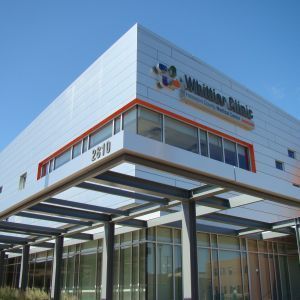 Whittier Clinic building exterior with large windows, silver facade, and orange accents under a blue sky.