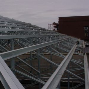 Steel roof trusses being assembled on a building under construction, cloudy sky in the background.