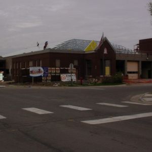 Building with construction on roof and brick exterior at intersection. Crosswalk in foreground.