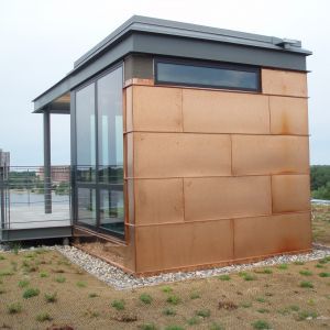 Small copper-clad building with glass walls and a dark roof, on a green rooftop.