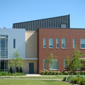 Modern brick and white building with a slanted metal roof and green lawn on a sunny day.