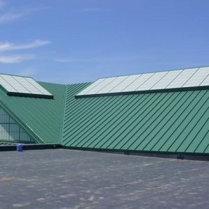 Green metal roof with skylights against a blue sky, viewed from a flat black roof.