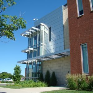 Modern building with metal and glass facade, red brick wall, blue sky, and landscaping.