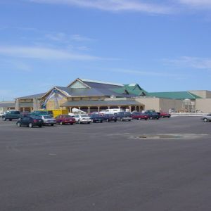 Large building with a complex roof and a parking lot filled with cars on a sunny day.
