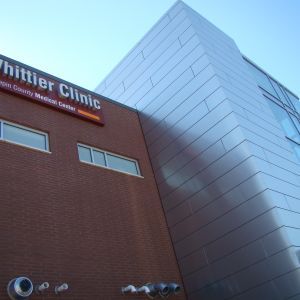 Whittier Clinic building with red brick and silver metal exterior against a blue sky.