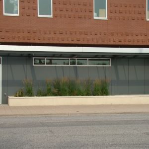 Building with brick upper level, gray lower level, windows, and plants in a planter.