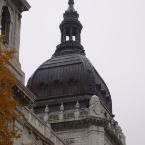 Dark dome atop a light-colored building, topped with a smaller turret, under a cloudy sky.