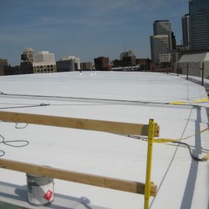 A white rooftop with safety railings, a bucket, and a cityscape in the background.