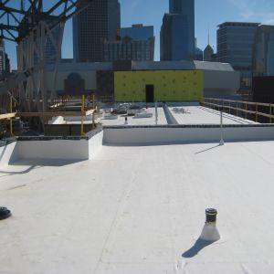 White flat roof with city skyline in the background, a yellow wall, and construction materials.