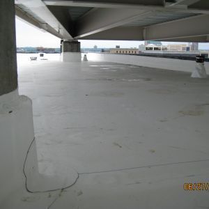 White rooftop under a metal beam; urban setting with buildings in the background.