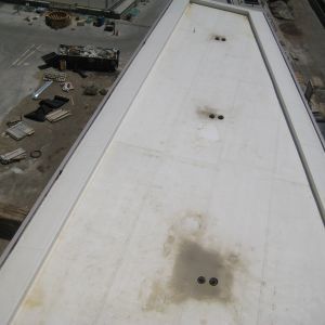 White, angled rooftop with several dark drain openings. Bordered by white edges, with a construction site visible.