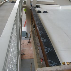 Construction worker on a rooftop installing a railing with a black waterproof membrane.