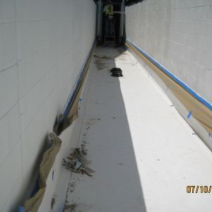 Narrow trench with white walls, debris, and person working in the distance. Blue tape lines the edges.