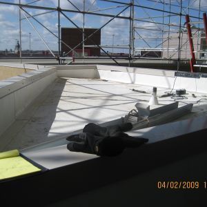 Construction site: White-walled structure on a rooftop, scaffolding, gloves and tools.
