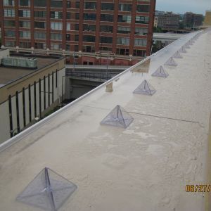 A building rooftop with several small, clear pyramid-shaped structures. Gray, wet surface. City backdrop.
