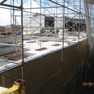 Construction site with scaffolding around a concrete structure. Workers visible in background.