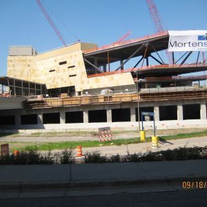 Construction site of a modern building with red cranes, concrete structure, and rectangular windows.