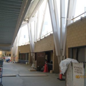 Interior view of a building under construction, featuring angled support beams and large windows.