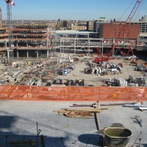 Construction site with multiple cranes and buildings under construction; orange safety fence.
