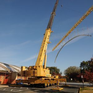 Yellow crane lifting a curved metal structure on a sunny day.