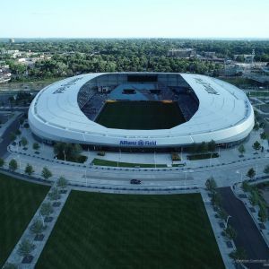 Aerial view of Allianz Field soccer stadium in St. Paul, Minnesota, with green field, white roof, and surrounding cityscape.