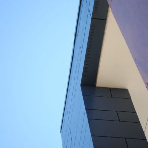 Modern building exterior against a blue sky, featuring dark gray paneling and a white ceiling.