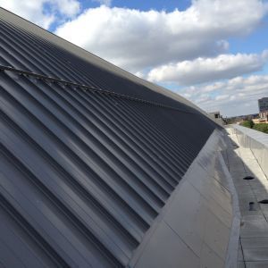 Curved, gray metal roof with ridged panels against a partly cloudy sky.