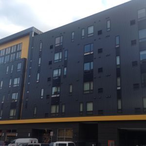 Modern multi-story building with dark gray exterior and yellow accents, several windows.