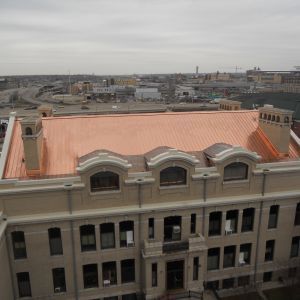 Building with copper roof, windows, and ornate details, overlooking a city on a cloudy day.