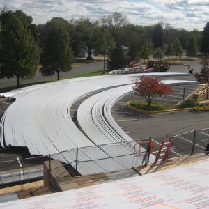White roofing material laid out in a curving pattern across a parking lot for installation.