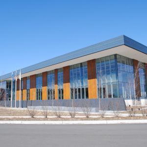 Modern building with glass windows, wood panels, and a blue roof under a clear, blue sky.