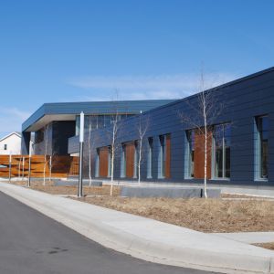 Modern blue building with large windows, brown accents, and a sidewalk.
