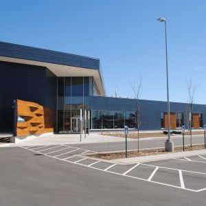 Modern, blue building with glass entrance, parking spaces in front under a clear sky.