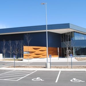 Modern building with dark blue exterior, wooden accents, and accessible parking spaces.