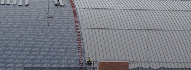 View of a rooftop with a metal sheet construction. A red ladder leads up to the roof. A person is near the chimney.