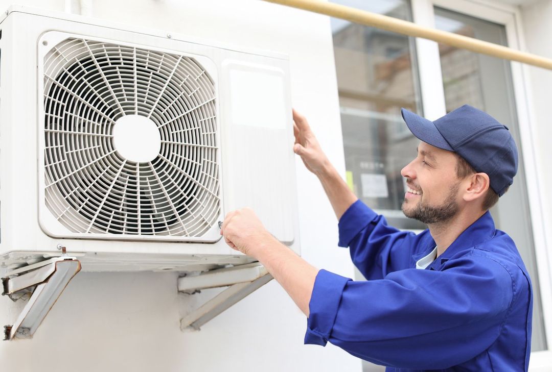 A man is installing an air conditioner on the side of a building.