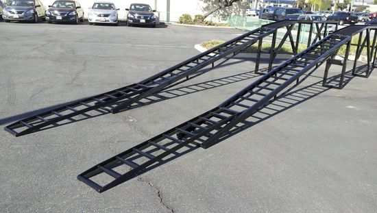 A car ramp is sitting in a parking lot with cars parked behind it