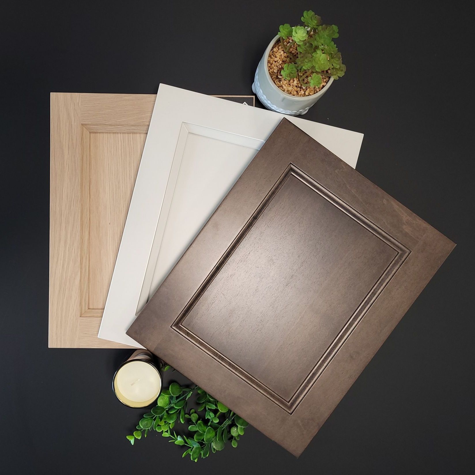 Échantillons de portes d'armoires : grain de bois, blanc et marron sur une surface noire avec des plantes.