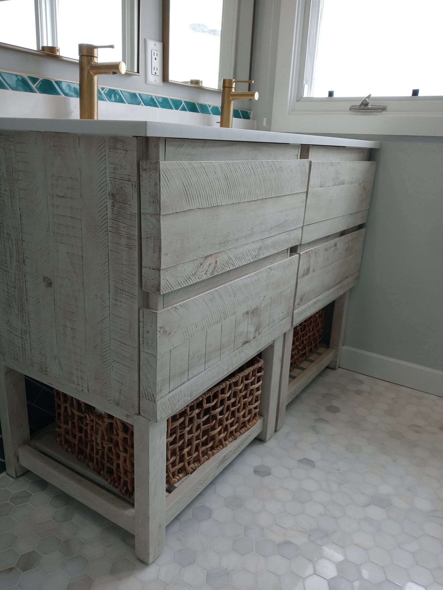 Rustic white wood bathroom vanity with drawers, wicker baskets, and gold faucets.