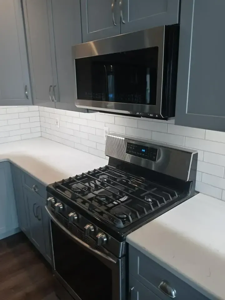 Gray kitchen with white countertops and subway tile backsplash; stainless steel range and microwave.