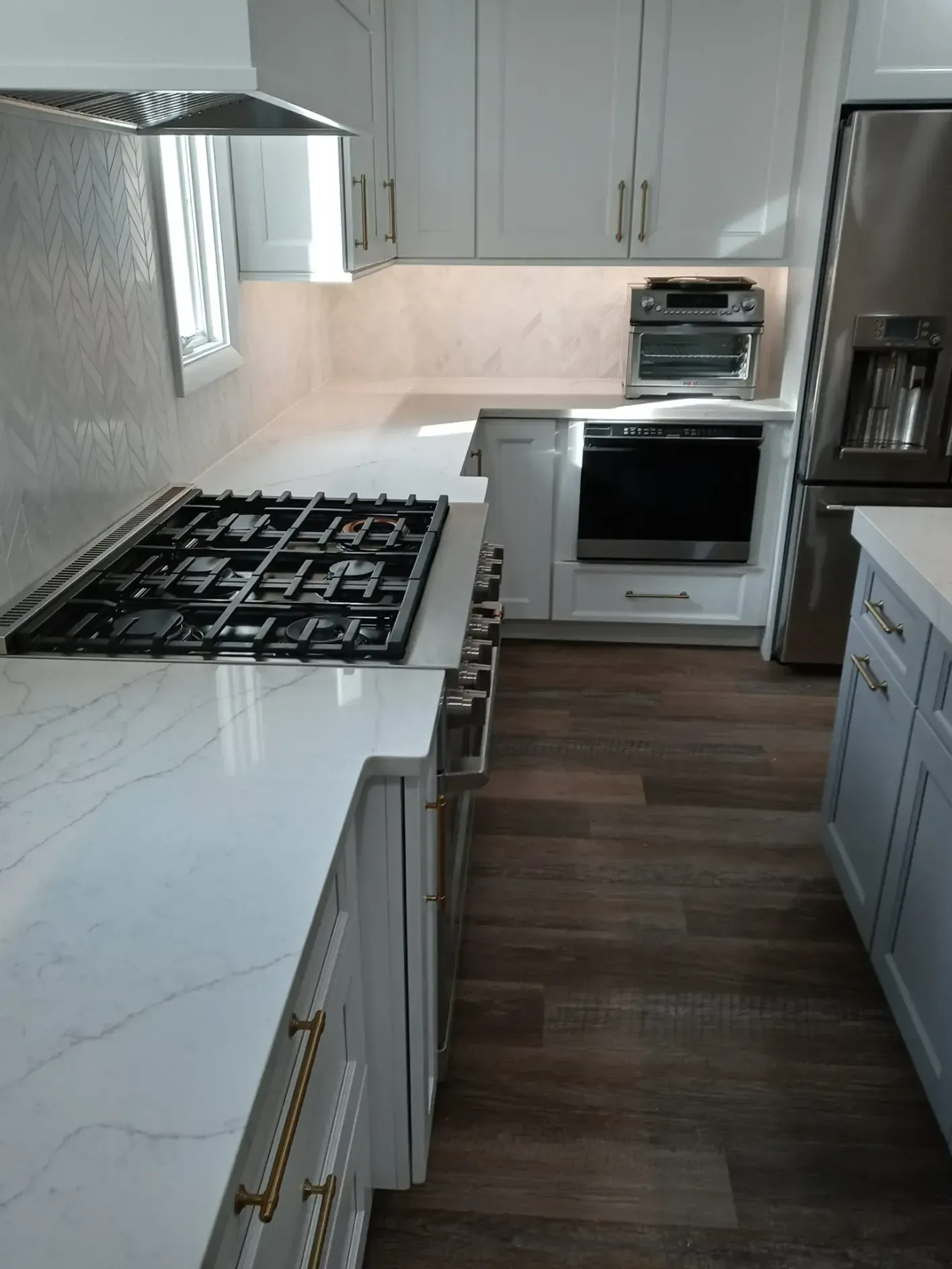 Modern kitchen with white cabinets, marble countertops, stainless steel appliances, and wood flooring.