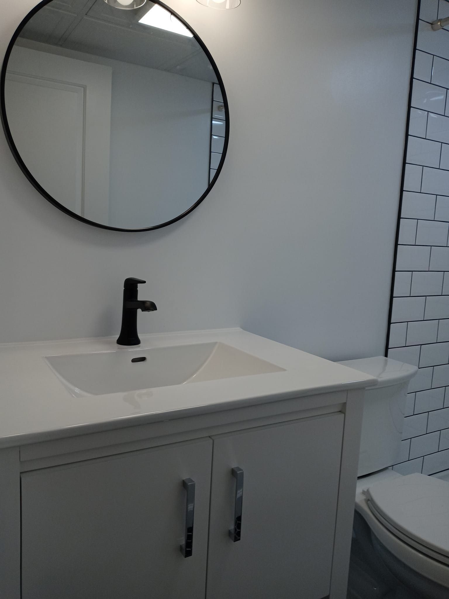 White bathroom with a white sink, black faucet, and round mirror.