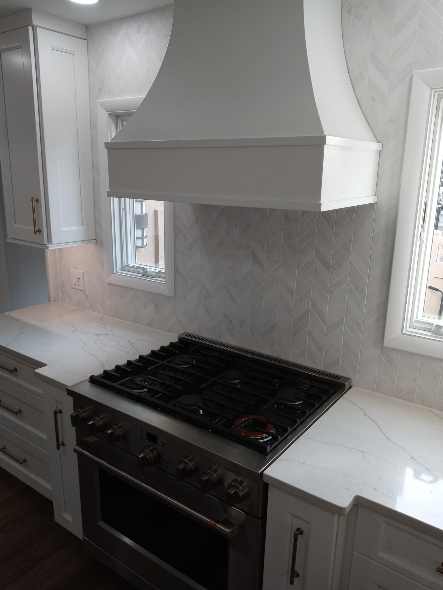 White kitchen with stove, range hood, cabinets, and backsplash.
