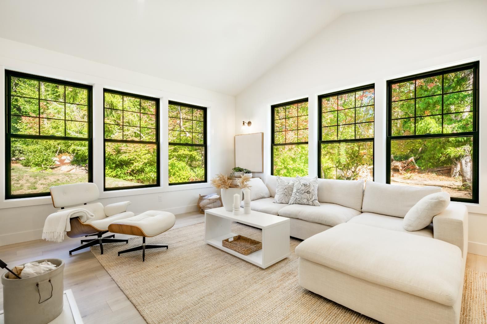 White living room with large windows overlooking trees; white sectional sofa, chair, and coffee table.