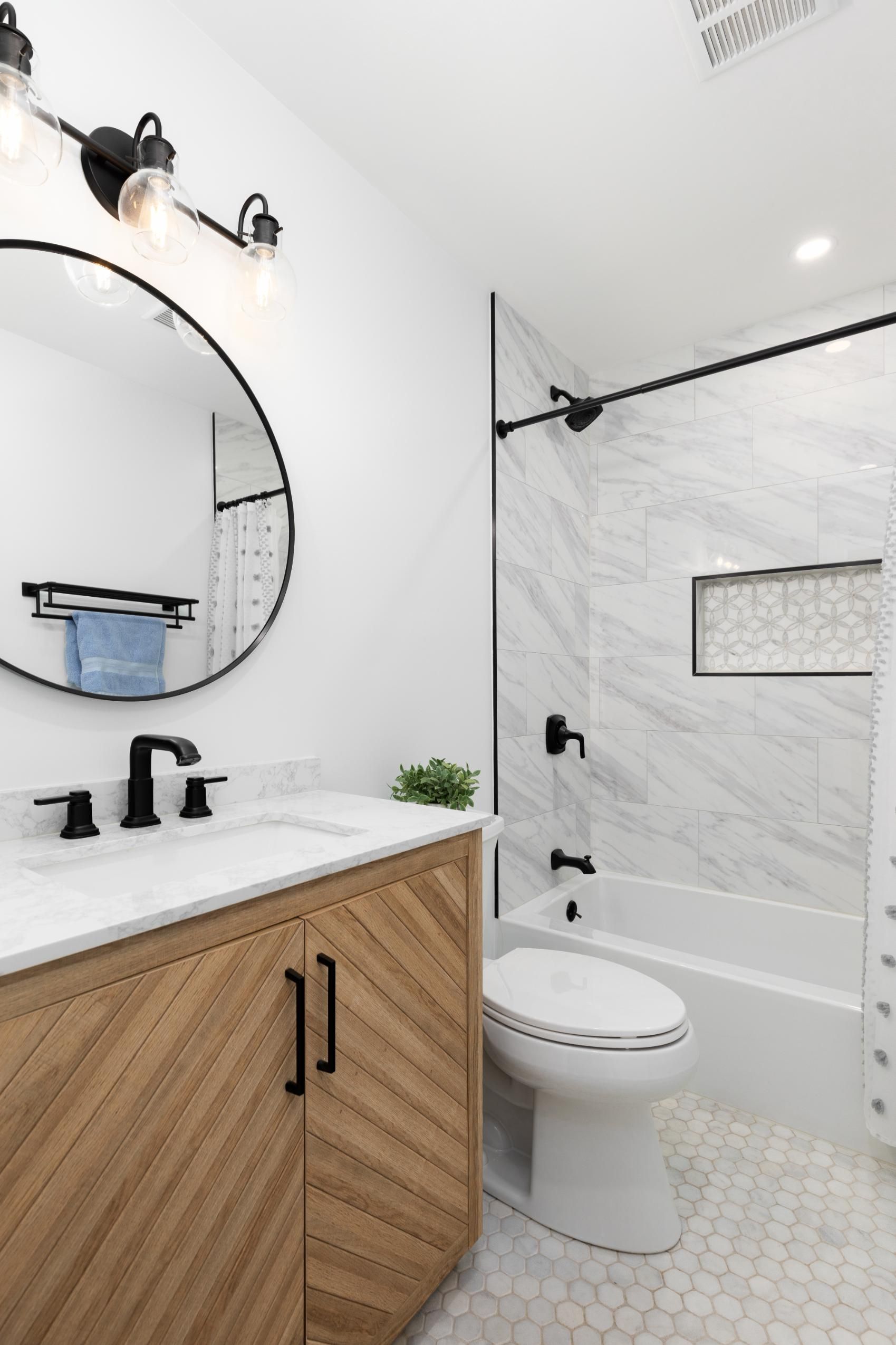 Bathroom with wood vanity, round mirror, white tile, black fixtures.