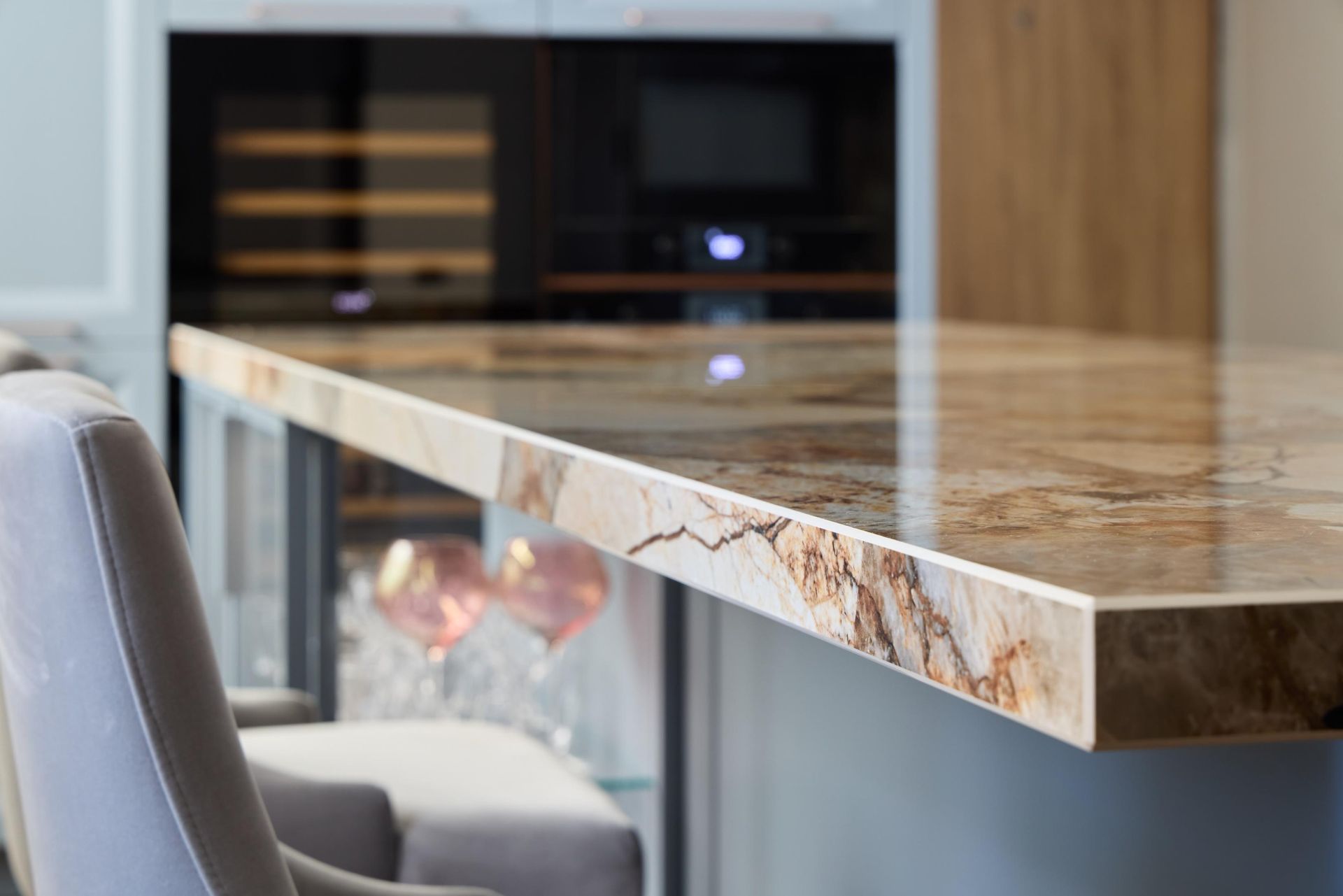 Close-up of a kitchen countertop made of patterned marble. Wine cooler, microwave, and a bar stool are in the background.