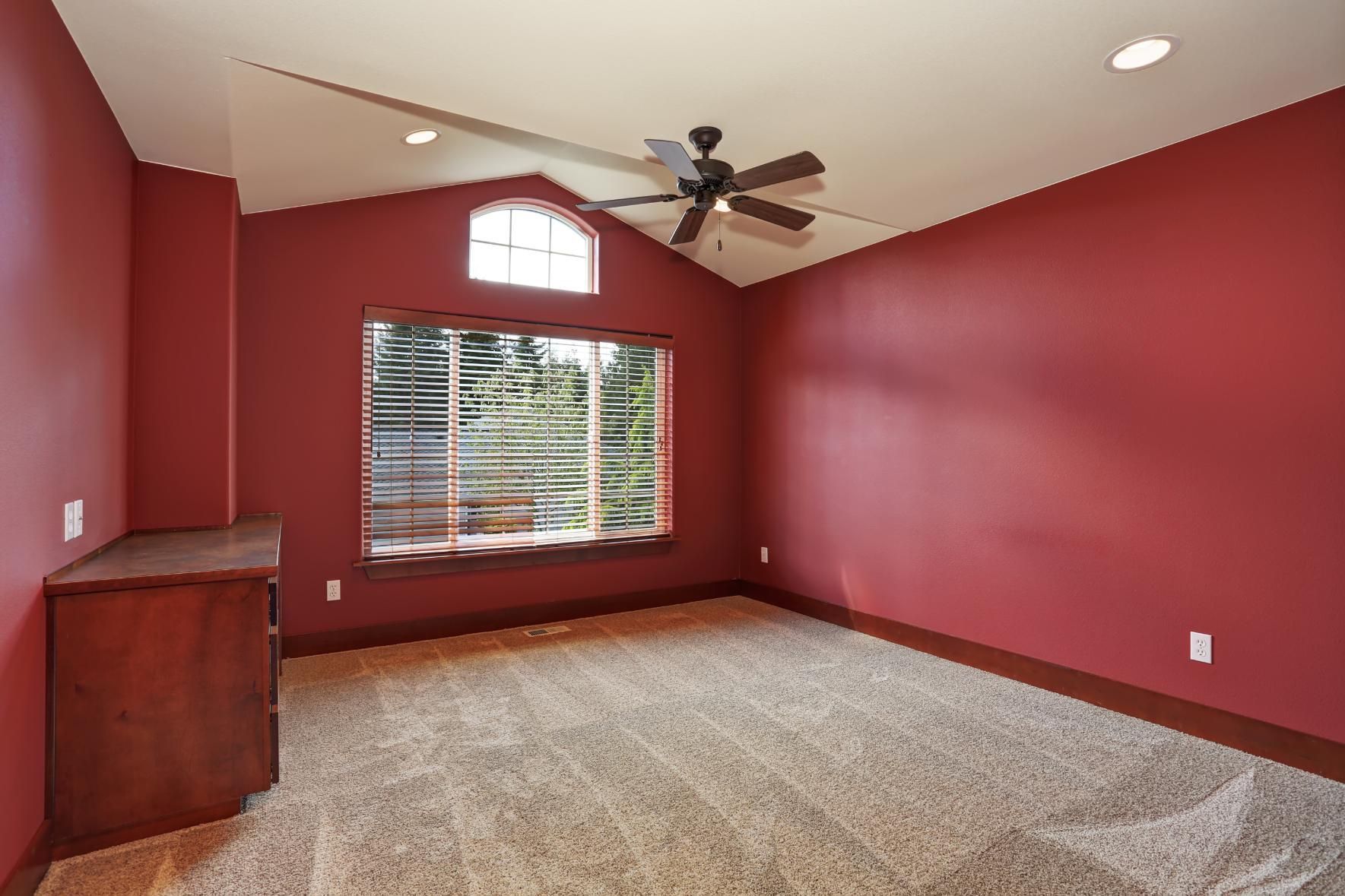Empty room with red walls, carpet, window, ceiling fan, and built-in wood cabinet.