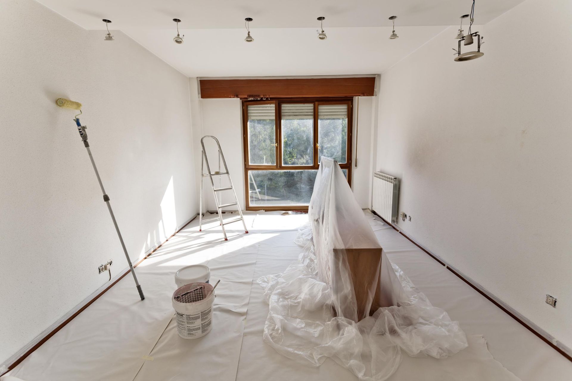 Room being painted, with white walls, drop cloths, and painting supplies.