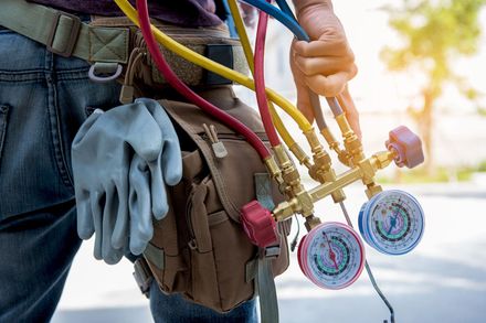 Worker holding manifold gauges and tools beside a service belt Worker holding manifold gauges and tools beside a service belt